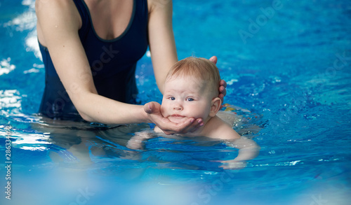 Little infant swimmer. Cropped view of mother standing in water and training her newborn baby floating in swimming pool. Baby diving in water. Early sport activity from first year of life