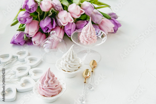 Pink homemade meringues on a white table with a bouquet of pink tulips. Gift set. Copy space