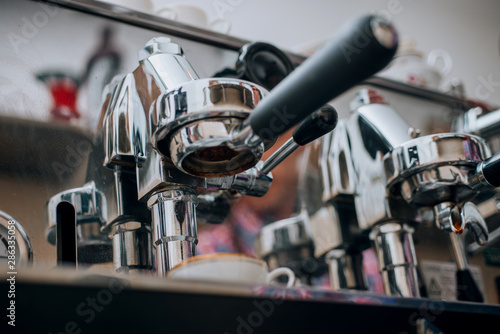 Coffee being brewed by the machine flowing through portafilter into the cup at cafe