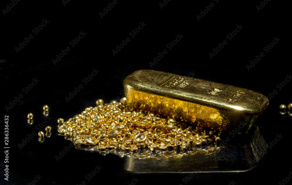 Gold bar on a pile of gold granules. Isolated on a black background. Gold bar on a pile of gold granules. Isolated on a black background.