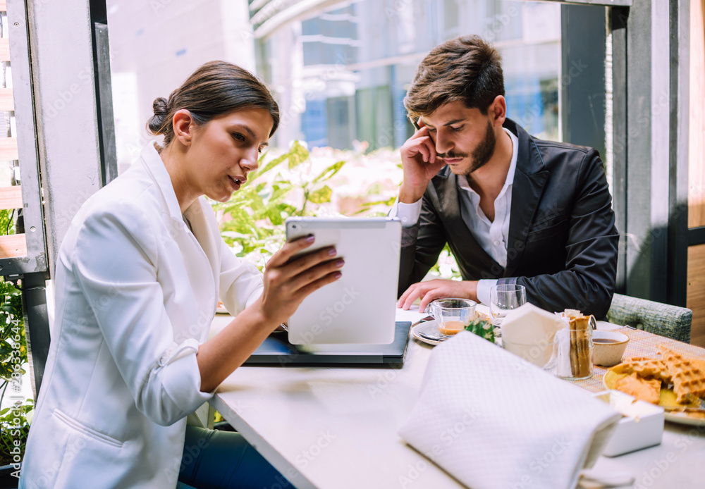 Two modern businessmen sitting at table and discussing strategy while using pc tablet Two modern businessmen sitting at table and discussing strategy while using pc tablet