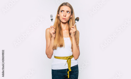 Diet concept. Attractive young blonde woman holds spoon and fork in hands with measuring tape on body