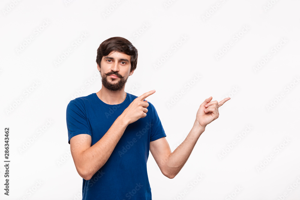 Handsome brunet man in a blue shirt with beard and mustaches pointing with his fingers to the right corner standing isolated over white background. Place of product and advertisment. Handsome brunet man in a blue shirt with beard and mustaches pointing with his fingers to the right corner standing isolated over white background. Place of product and advertisment.