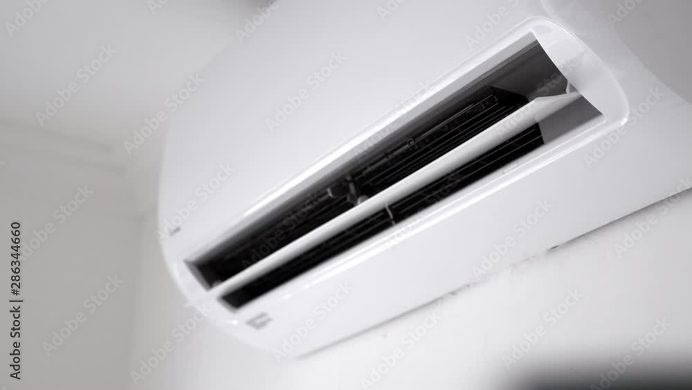 Flat air conditioner on white wall in room interior. Man pushing button on remote. Setting temperature Flat air conditioner on white wall in room interior. Man pushing button on remote. Setting temperature