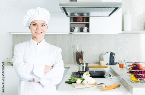Young female chef in white uniform standing near workplace