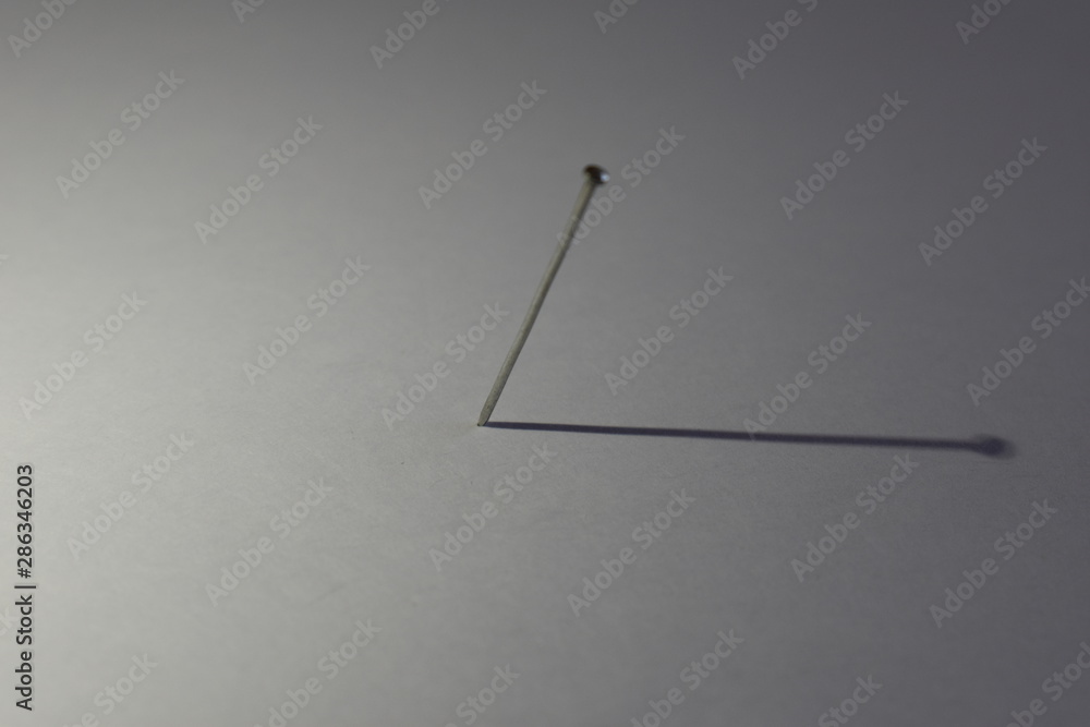 A nail on a light background with its shadow depicts a clock hand A nail on a light background with its shadow depicts a clock hand