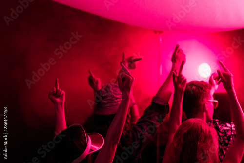 back view of people with raised hands during rave party in nightclub