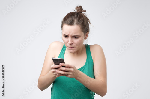 Young caucasian woman in green shirt looking at phone with irritation. Virus on her phone concept.