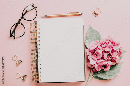 Female workspace with laptop, pink hydrangea, golden accessories, pink diary on pink background. photo