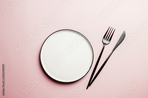 Black setting: plates, inen napkin and silverware on pink background. Top view.