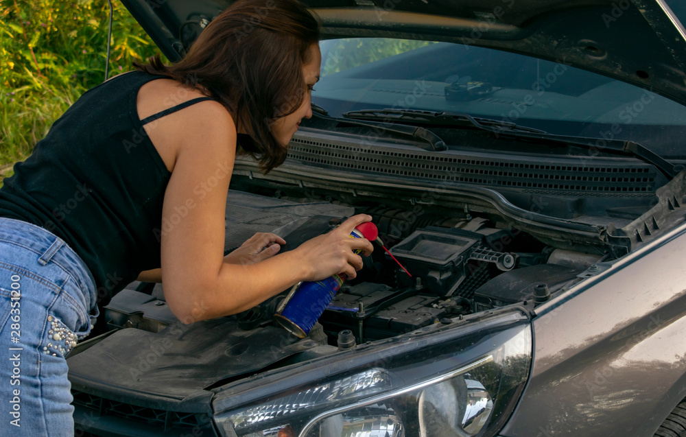 A beautiful young girl tries to change the spark plugs in the car, but does not know how to do it. A beautiful young girl tries to change the spark plugs in the car, but does not know how to do it.