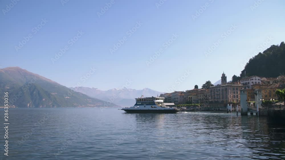 Ferry boat on water by pier lakeside town of Bellagio on Como lake in Lombardy Italy, view of medieval city harbor on beautiful mountain lake. Early morning sunny day Ferry boat on water by pier lakeside town of Bellagio on Como lake in Lombardy Italy, view of medieval city harbor on beautiful mountain lake. Early morning sunny day