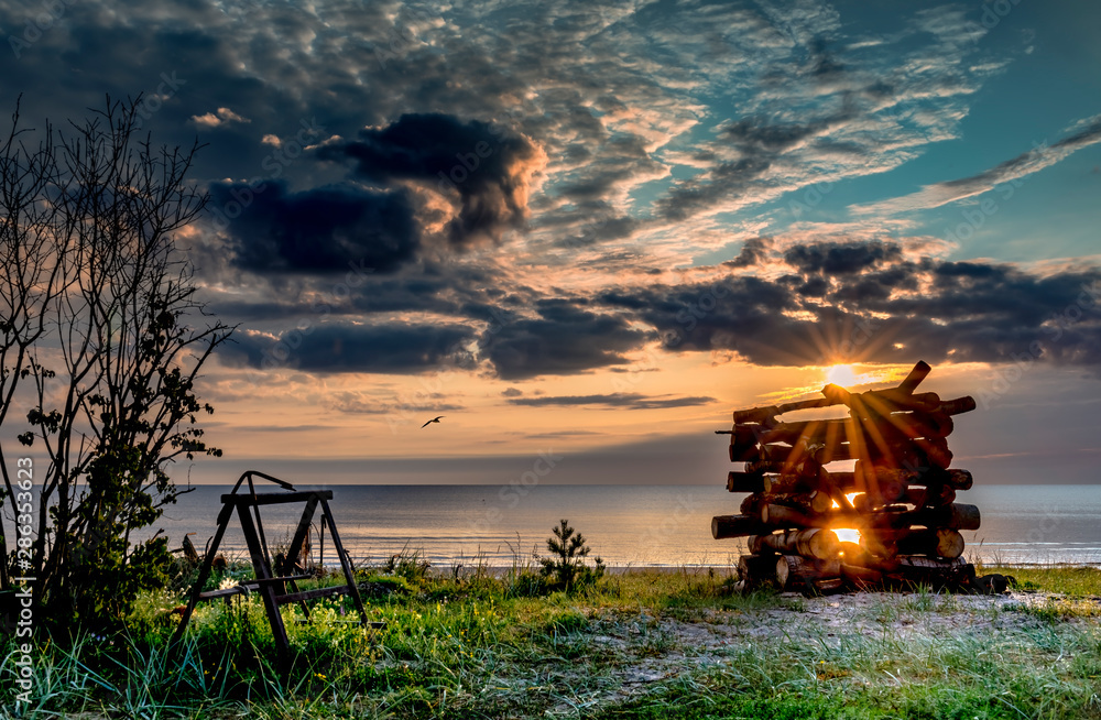 Fototapeta premium Coastal landscape on a beach of the Baltic Sea. Wooden log deck for a fire that will be used as a symbol of traditional Latvian holiday of summer solstice - Ligo