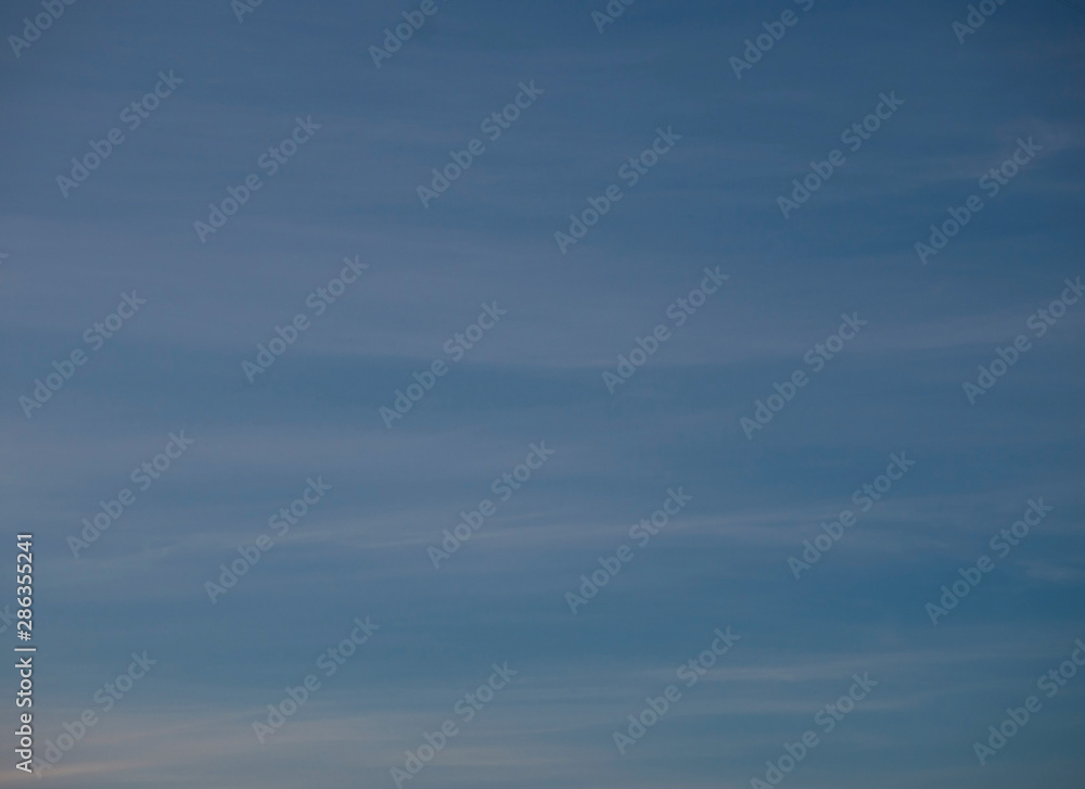 Blue sky with thin white stripes of clouds background. Beautiful panoramic sky with upcoming twilight.