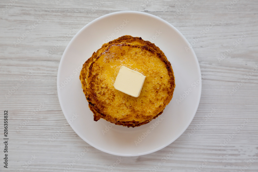 Top view, homemade corn meal Johnny cakes with butter on a white plate on a white wooden background. Flat lay, overhead, from above. Close-up.