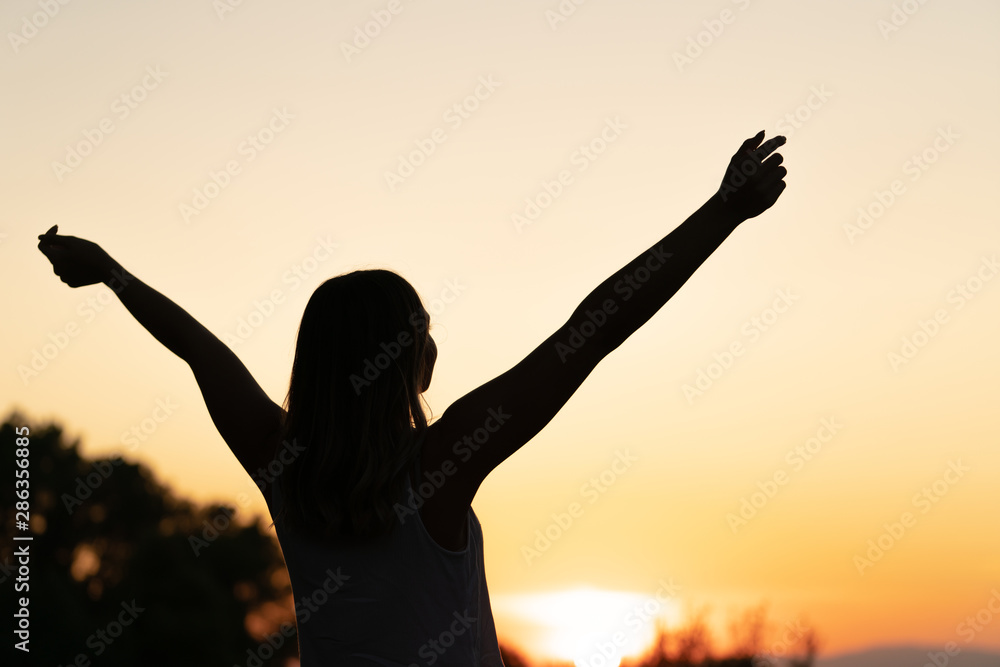 silhouette of young woman with open arms raised in a sunset