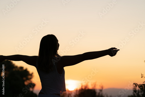 silhouette of womasilhouette of young woman with open arms raised in a sunsetn relaxing her arms at sunset photo