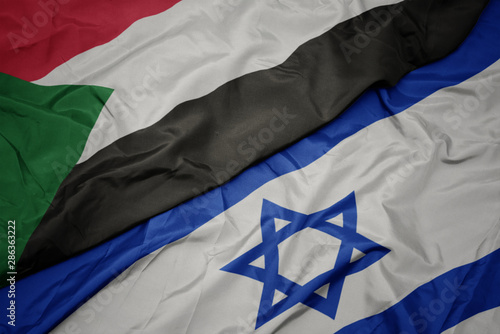 Fototapeta waving colorful flag of israel and national flag of sudan.