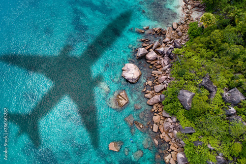 Concept of airplane travel to exotic destination with shadow of commercial airplane flying above beautiful tropical beach. Beach holidays and travel.