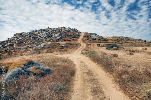 A winding country dirt road leading up a hill to a cloudscape, Naxos, Greek Islands