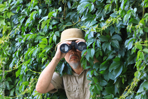 Photos traveler looks through binoculars in the leaves