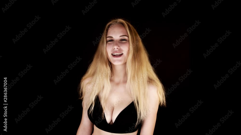 Lit from below, a busty blonde woman looks directly at the camera, laughing and shrugging suggestively Lit from below, a busty blonde woman looks directly at the camera, laughing and shrugging suggestively