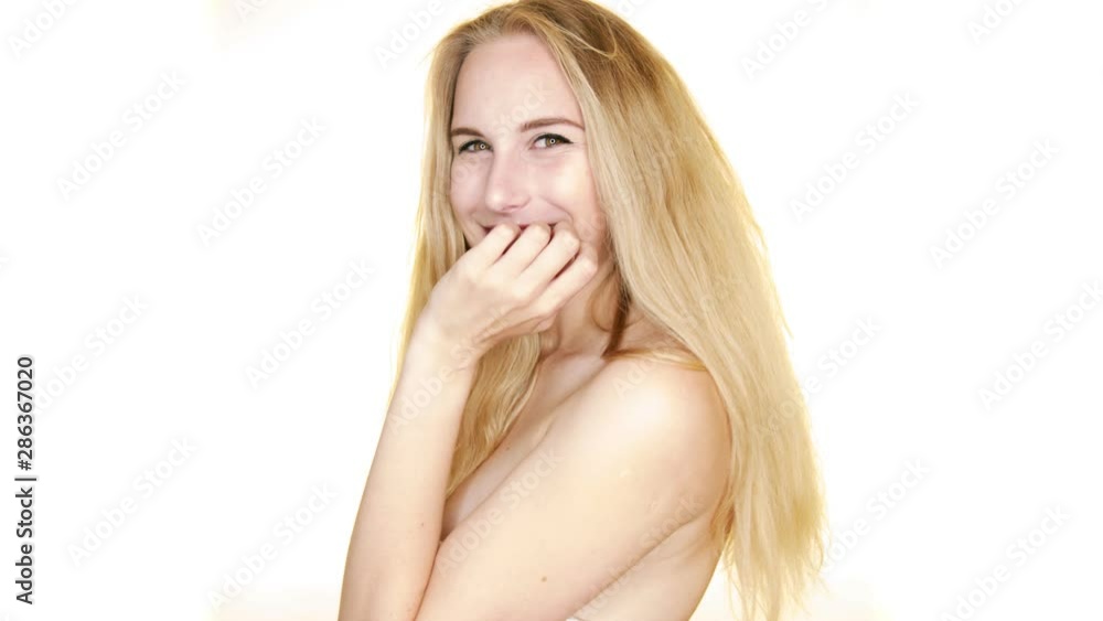 In slow motion, against a white backdrop, a young blonde woman looks over her bare shoulders and shrugs flirtatiously