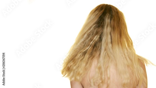 In slow motion, against a white studio background, a young blonde woman shakes her long hair from side to side photo