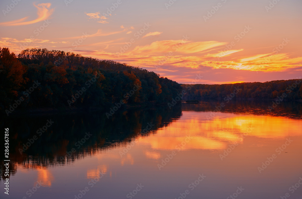 Obraz premium beautiful sunset in autumn season - trees silhouette near a river, bright sunlight