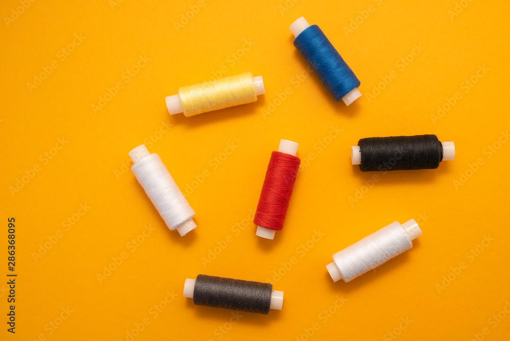 Set of sewing threads beautiful color (blue,yellow, green, white, black) on yellow background with space for text Set of sewing threads beautiful color (blue,yellow, green, white, black) on yellow background with space for text