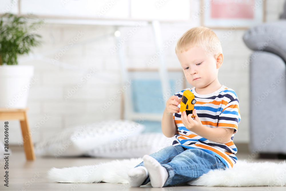 Little boy sitting on white carpet at home and playing with car toy Little boy sitting on white carpet at home and playing with car toy