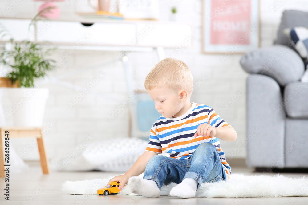 Little boy sitting on white carpet at home and playing with car toy Little boy sitting on white carpet at home and playing with car toy