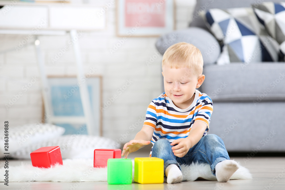 Little boy sitting on white carpet at home and playing with colorful plastic cubes Little boy sitting on white carpet at home and playing with colorful plastic cubes