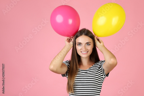 Young woman with colorful balloons on pink background