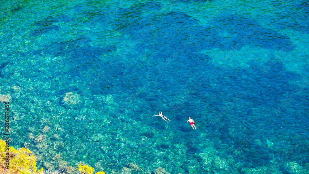 Fototapeta premium Two divers dive on the surface of the sea in a beautiful bay on a sunny summer day. Water activities, vacation at sea, happy holidays in the Mediterranean.