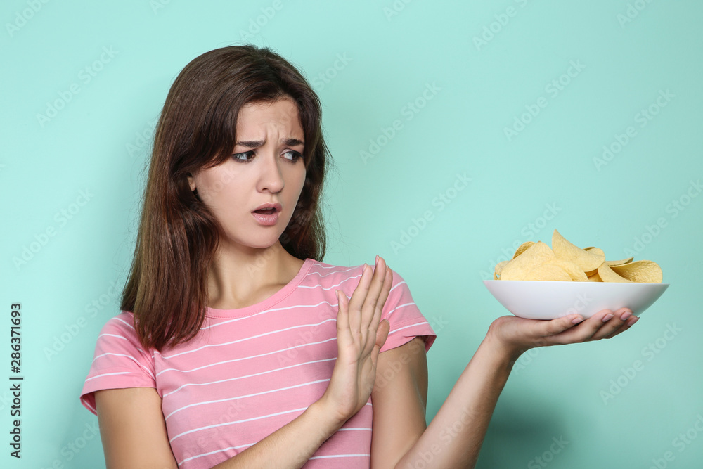 Young woman with potato chips in plate on mint background Young woman with potato chips in plate on mint background