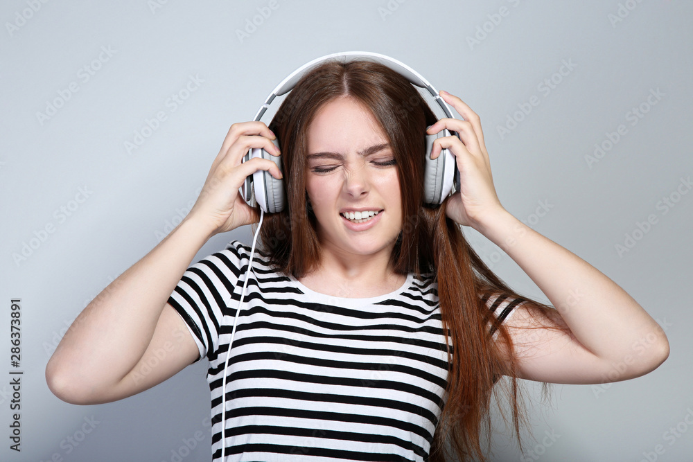 Naklejka premium Young beautiful woman with headphones on grey background