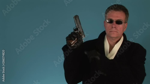 Man in a black trench coat cocking a 9mm pistol and looking at the camera