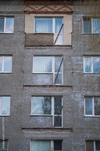 Broken concrete balcony on the facade of the building. Restoration of an old residential gray plastered house. Wooden windows and exit with door.