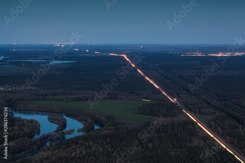 A small town in the distance among the forest. Village on the horizon in Taiga. Settlement in endless Tundra. The lights of the road at night near the pond. Evening river.