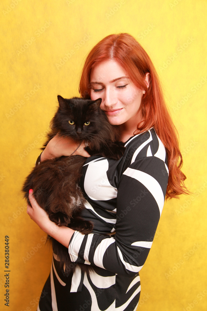 pretty young redheaded girl in long black and white dress with her lovely friend cat on yellow bright studio background pretty young redheaded girl in long black and white dress with her lovely friend cat on yellow bright studio background