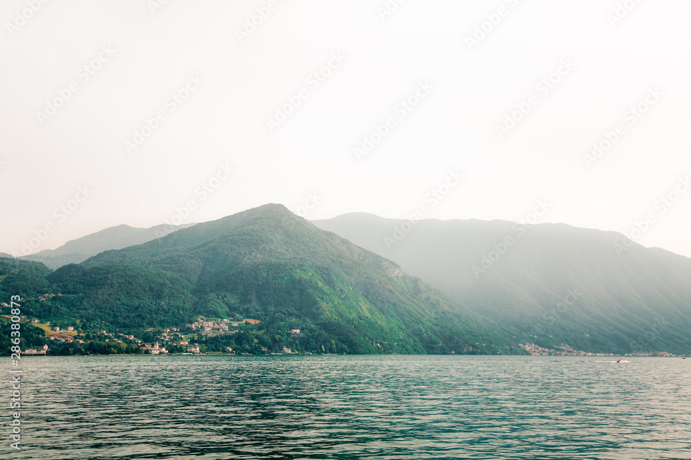 Lake Como (Italian Lago di Como) in summer. Foggy morning in Alps mountains.