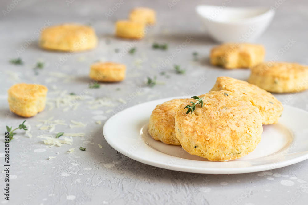 Savory scones or cookies with cheese and thyme on a white ceramic plate. Light grey concrete background. 