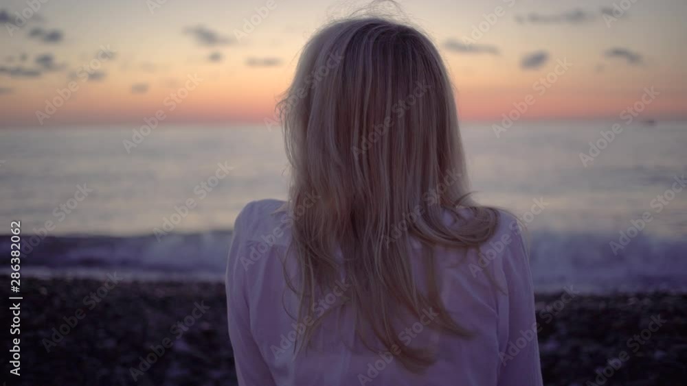 blonde woman, sitting on the shore, communicates using the application on a mobile phone, sunset, ocean, sea on the horizon. blonde woman, sitting on the shore, communicates using the application on a mobile phone, sunset, ocean, sea on the horizon.