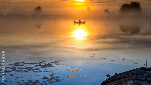 Sunrise with the mist above a river,  fisherman in a boat, summer morning in ...