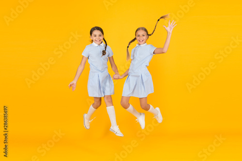 Little girls playing with cute braids. Beautiful schoolgirls. Back to school concept. Hairdresser salon. Cute schoolgirls. Girls with braided hair style. Cheerful schoolgirls yellow background photo
