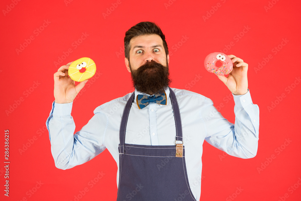 Catering bakery products to you. Bearded man holding ring donuts in bakery shop. Professional baker with glazed bakery food on red background. The perfect doughnuts from our bakery Catering bakery products to you. Bearded man holding ring donuts in bakery shop. Professional baker with glazed bakery food on red background. The perfect doughnuts from our bakery