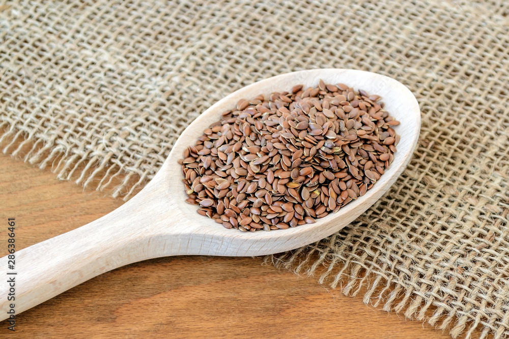 Whole flax seeds in a wooden spoon on a sackcloth background. Healthy food for lower cholesterol and preventing heart diseases. Whole flax seeds in a wooden spoon on a sackcloth background. Healthy food for lower cholesterol and preventing heart diseases.