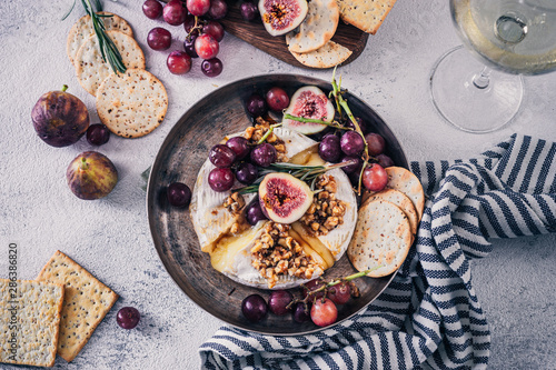 Fancy baked brie cheese platter with honey and walnuts, fresh rosemary. Red grapes, figs and white wine