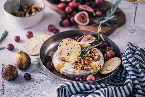 Fancy baked brie cheese platter with honey and walnuts, fresh rosemary. Red grapes, figs and white wine